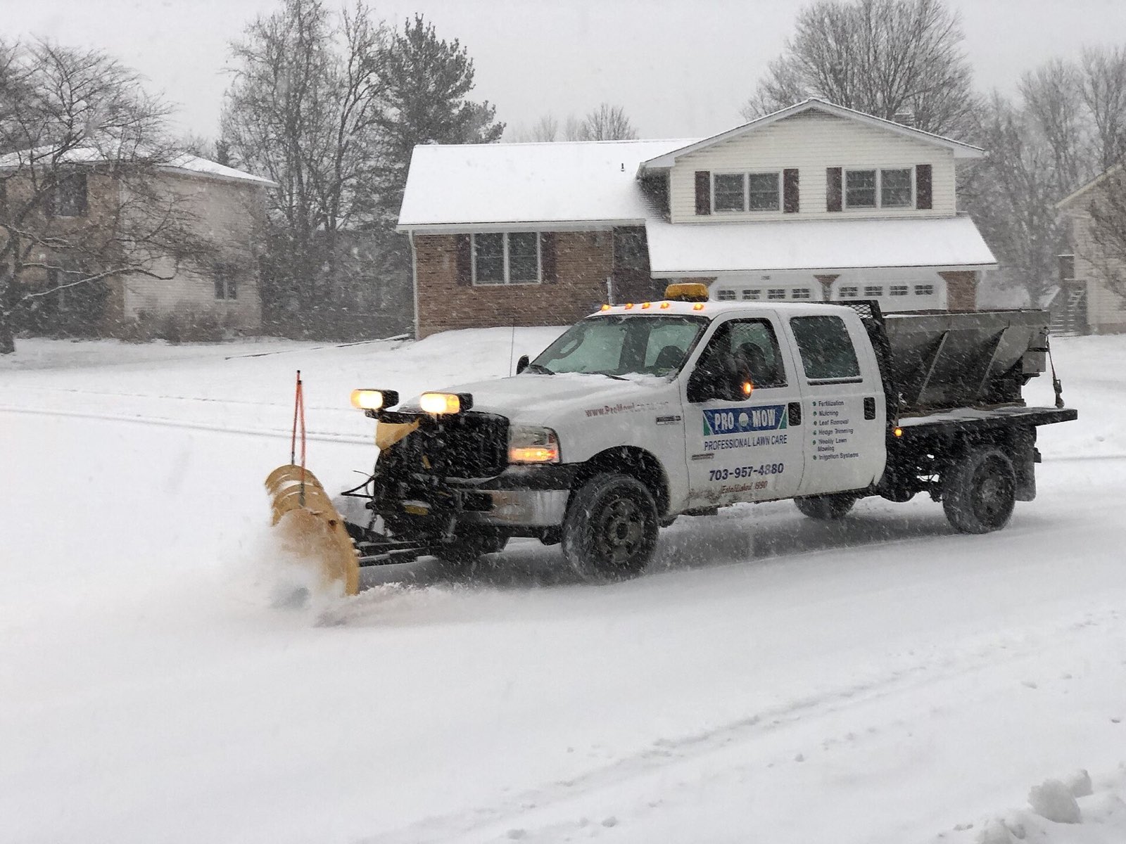 Pickup truck with plow and salter clearing the street in front of a house