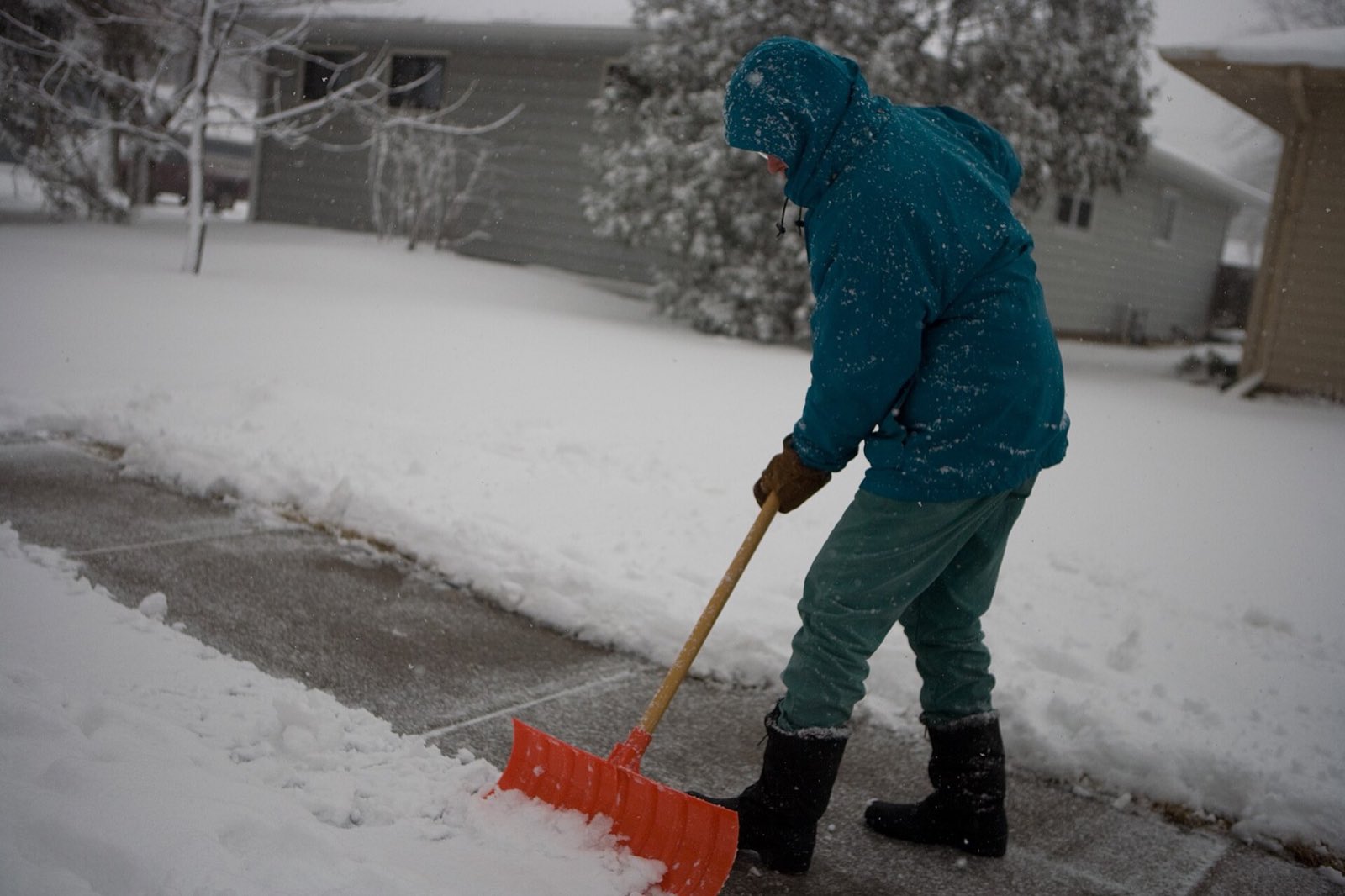Clearing a front walkway by hand with an orange shovel