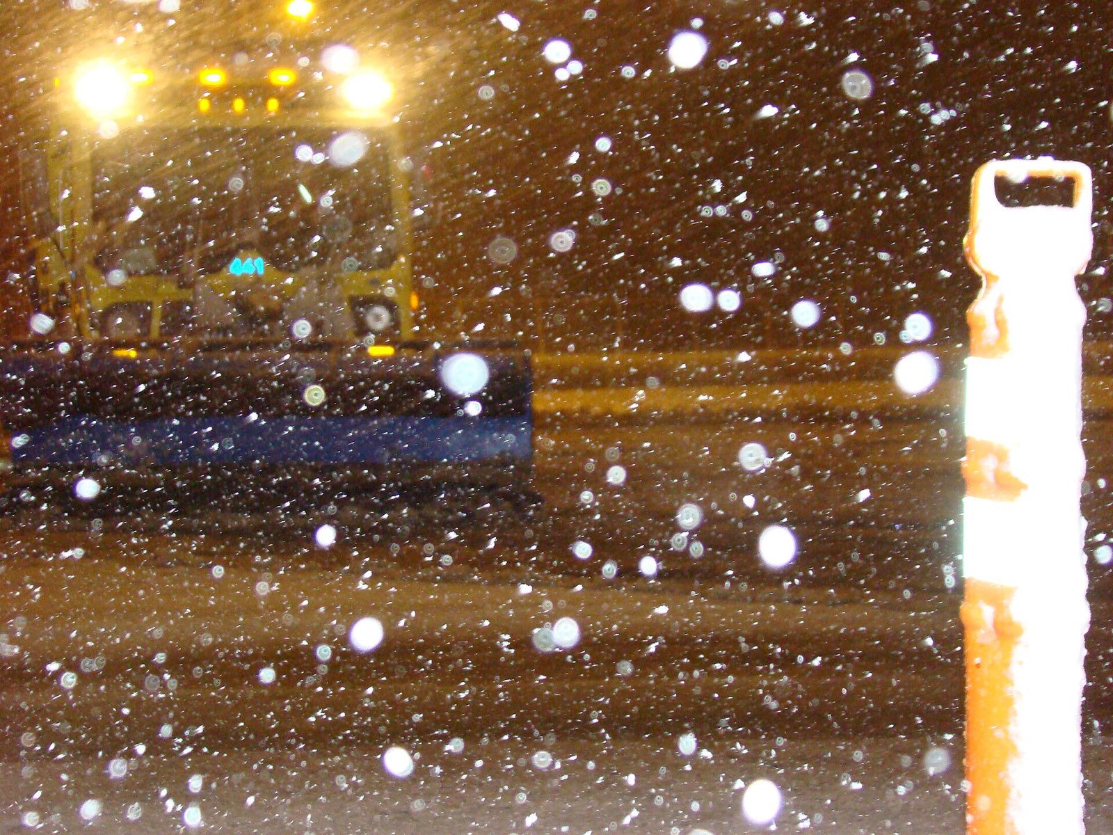 Plow truck in heavy snow at night, headlights catching the flakes